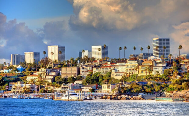 Coastal city skyline with boats on calm water under a dramatic cloud.
