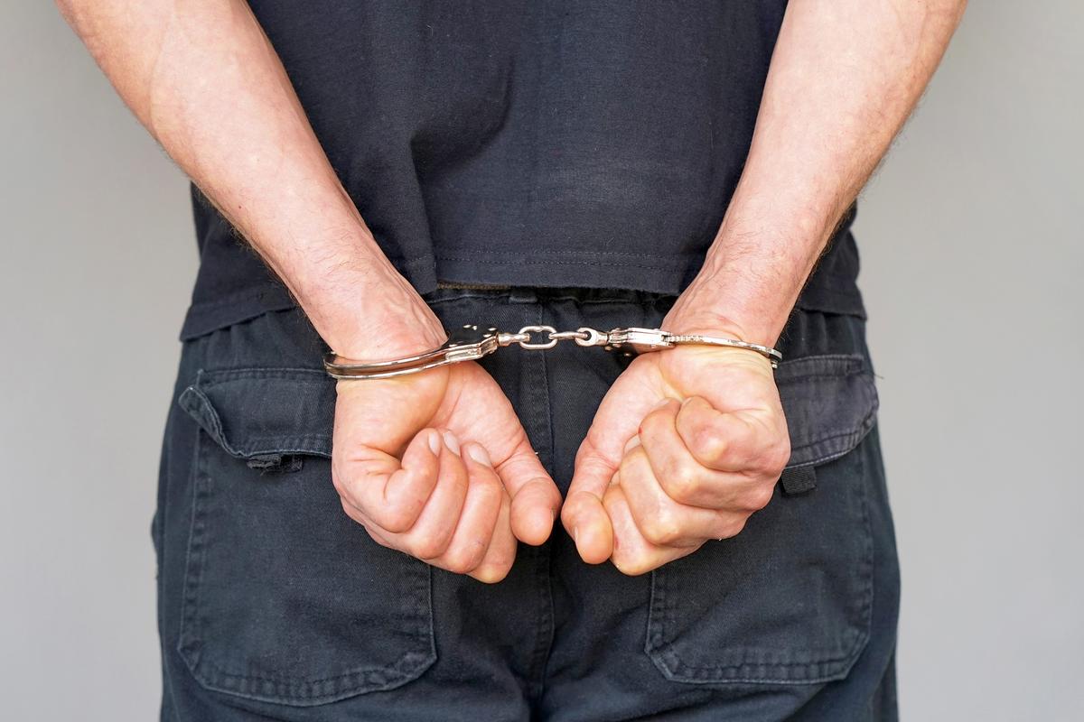 Close-up of a man's hands locked in handcuffs behind his back