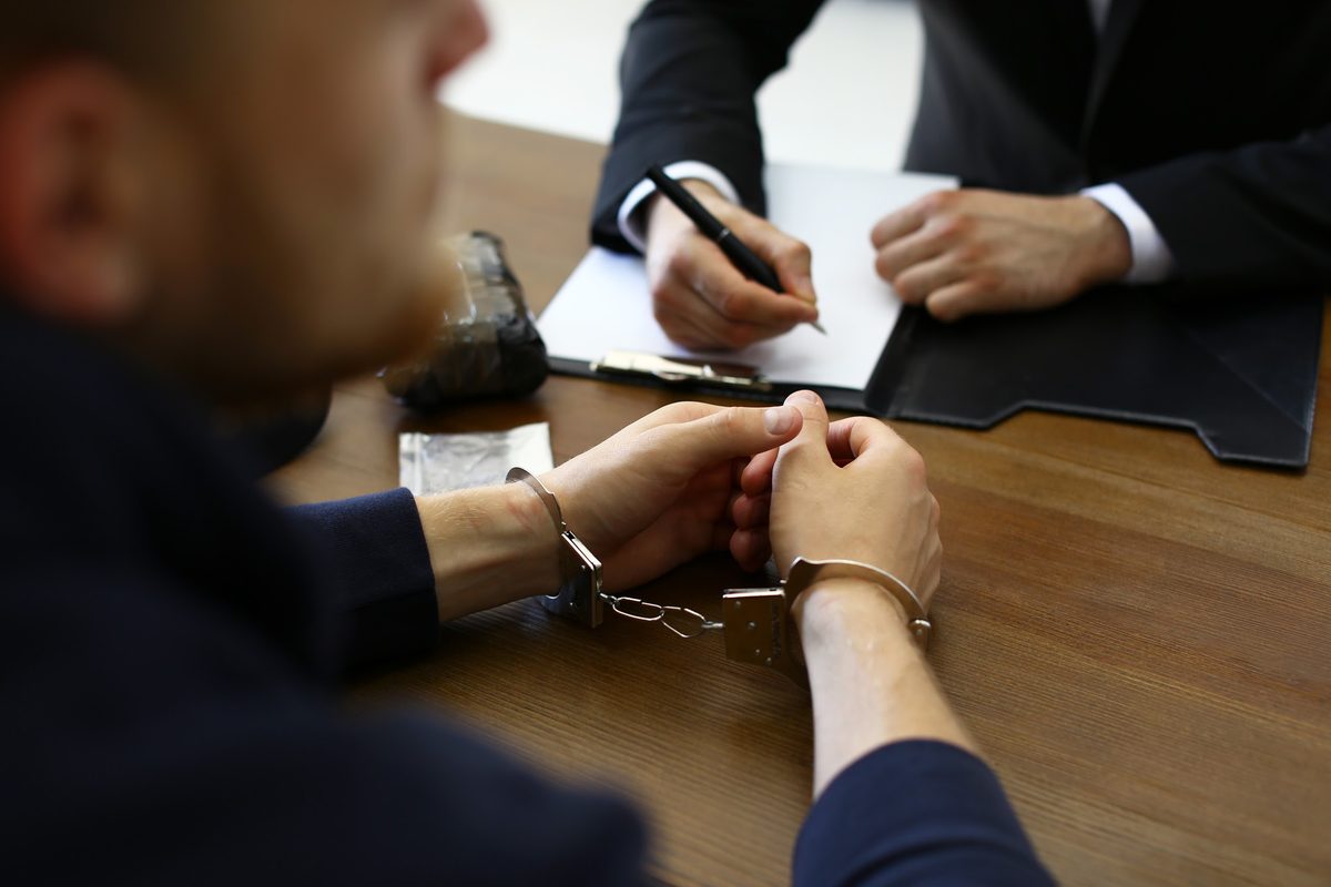 Handcuffed man at a desk while an agent writes up paperwork